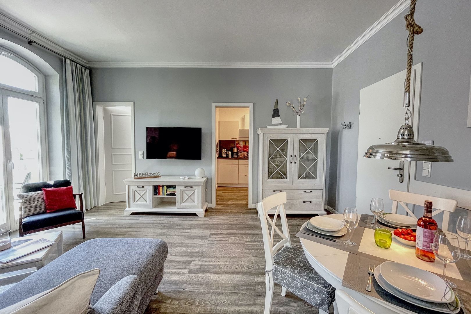 Wohnbereich eines Appartements mit hellem Holzboden, gedecktem Tisch und Fenster zum Balkon