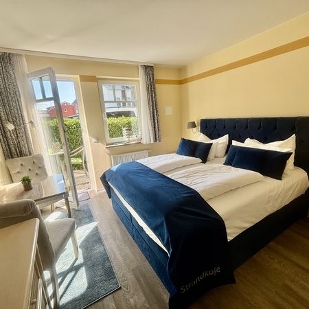Doppelzimmer mit Doppelbett, dunkelblauer Tagesdecke und geöffneter Balkontür zur Terrasse