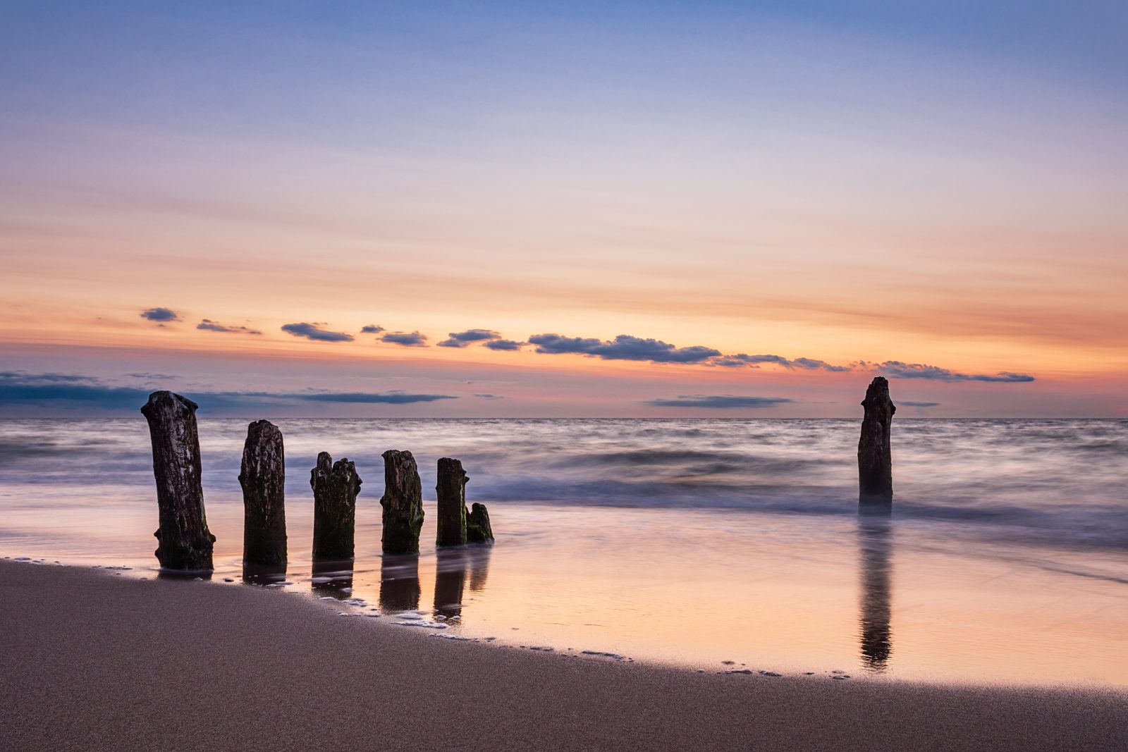 Buhnen im Sonnenuntergang, das Wasser spiegelt den rosa Abendhimmel
