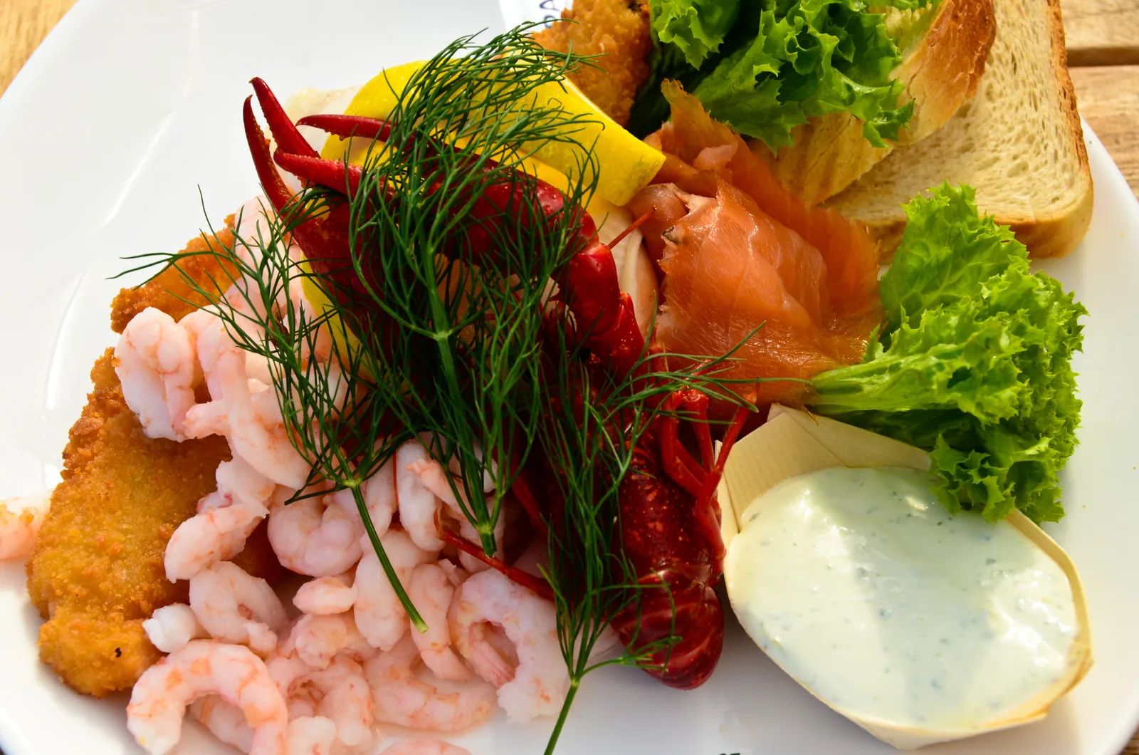Teller mit Krabben, Flusskrebs, geräuchertem Lachs, paniertem Fisch, Zitrone, Dill, Salat, Toast und Remoulade