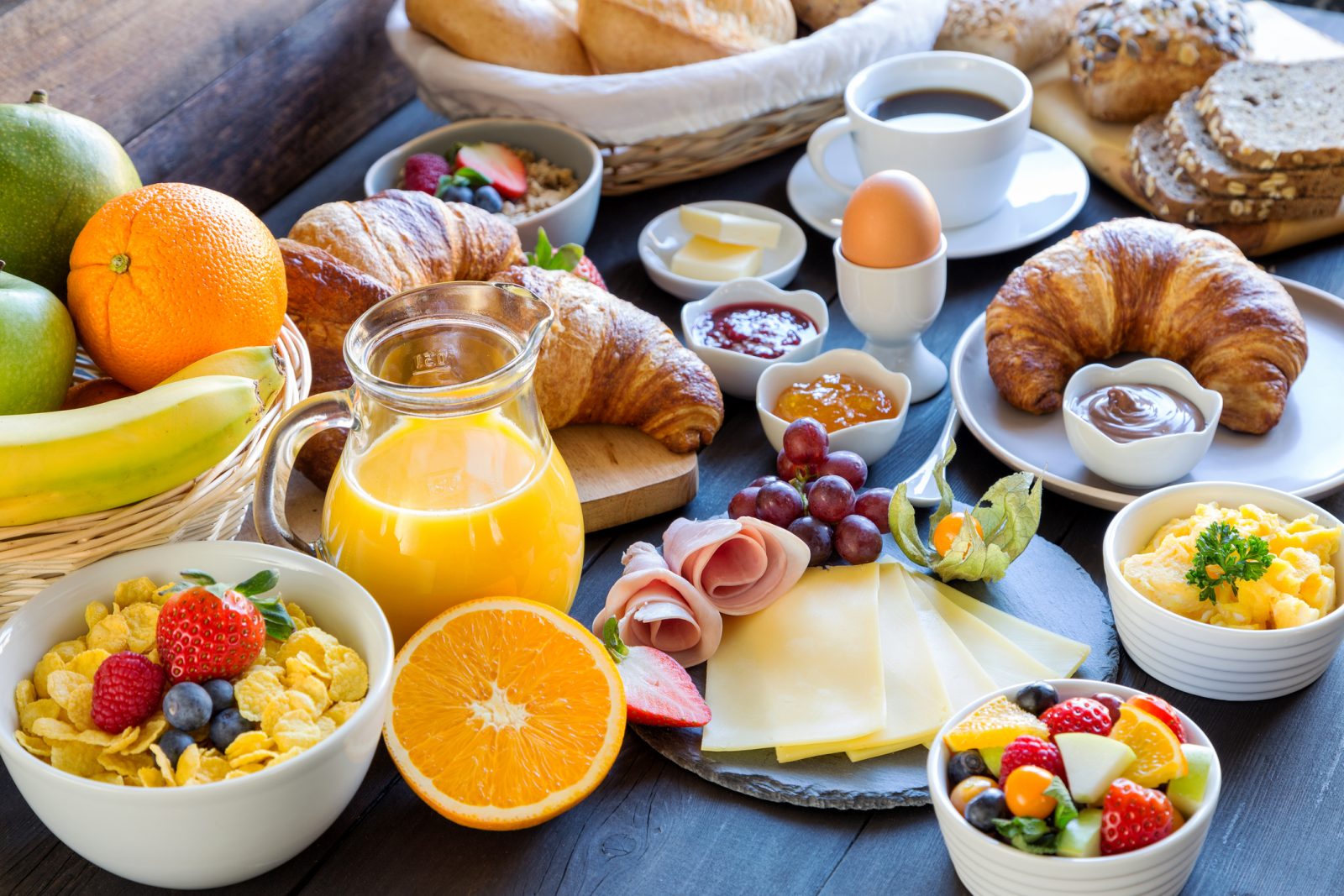 Frühstückstisch mit Croissants, Obst, gekochtem Ei und Orangensaft
