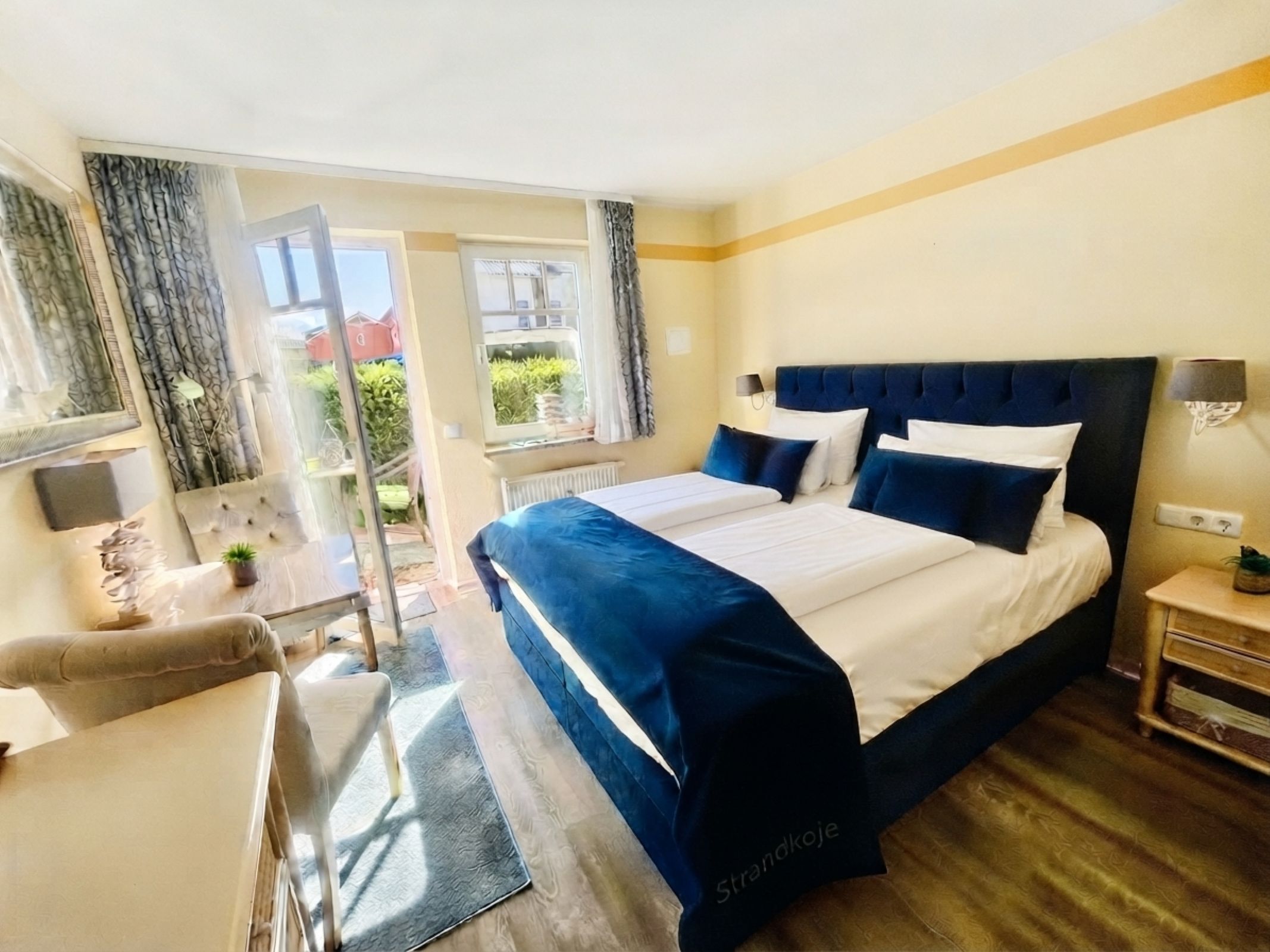 Doppelzimmer mit Doppelbett, dunkelblauer Tagesdecke und geöffneter Balkontür zur Terrasse